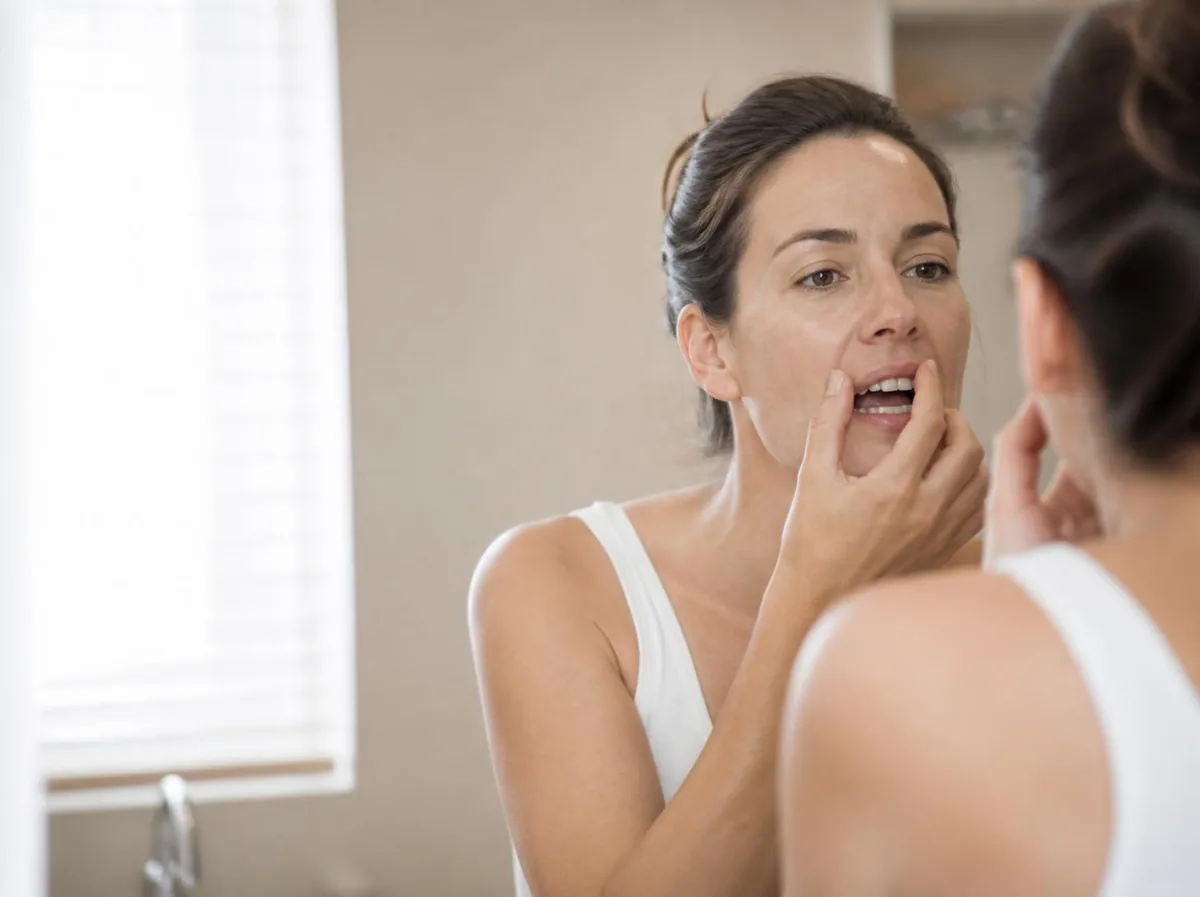 Woman checking gum recession in a mirror before treatment in Houston